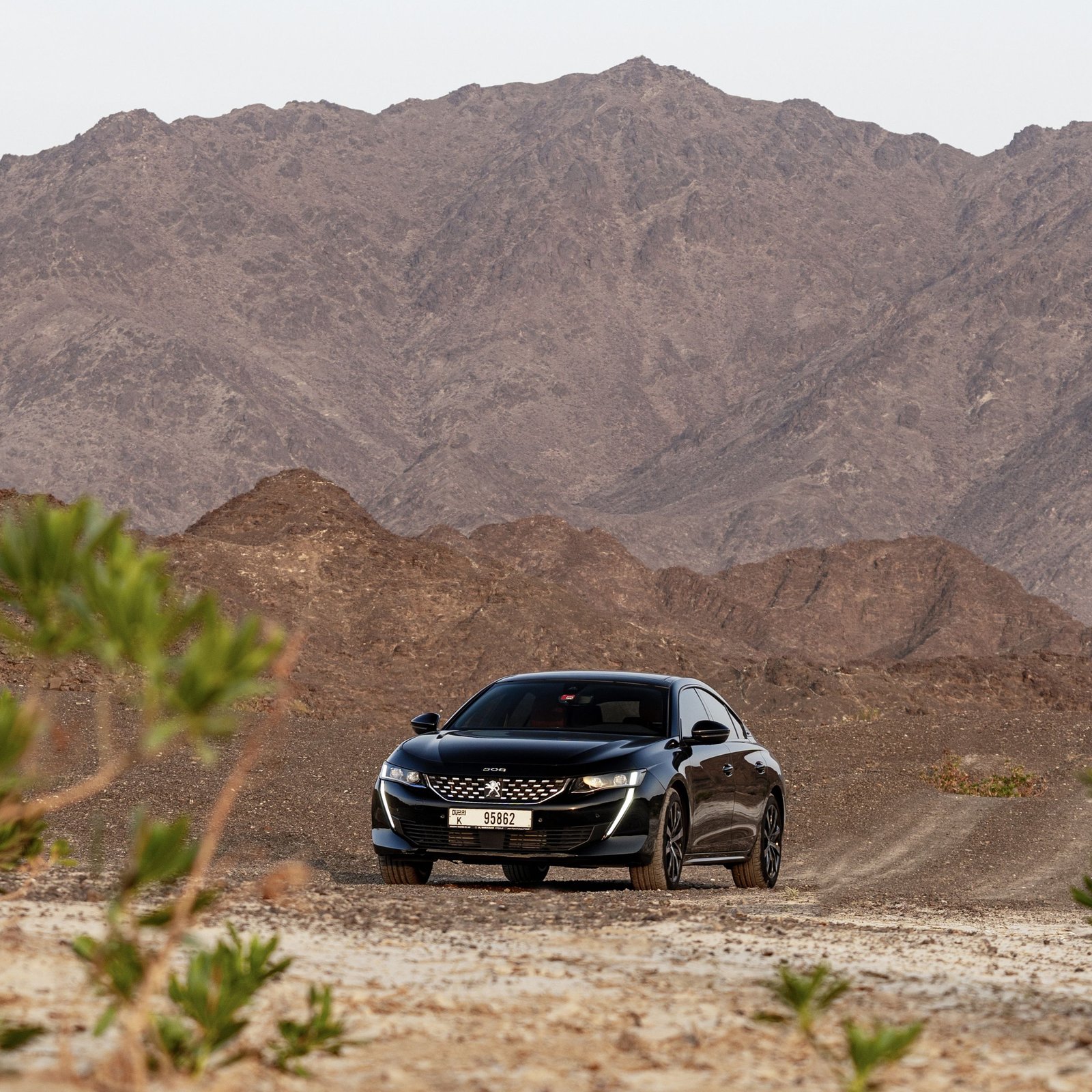A luxury sedan car driving on a dirt road amidst rocky desert mountains in Dubai.