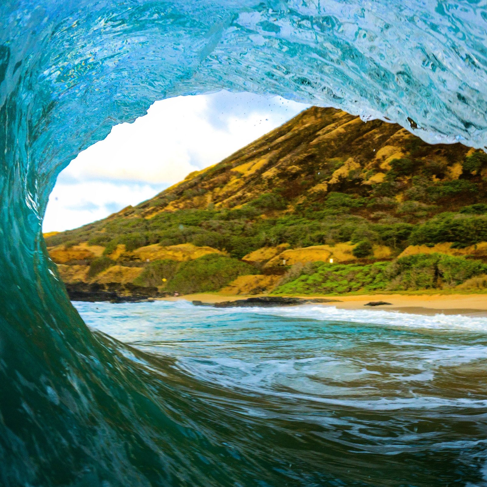 A captivating view through a wave tunnel showcasing a scenic beach and lush hillside.