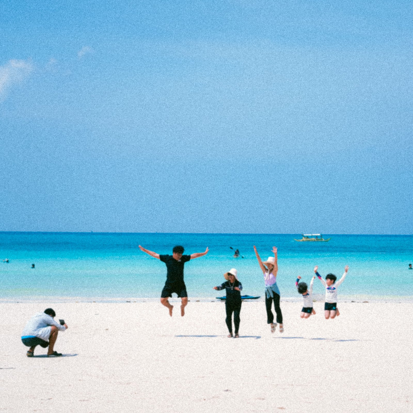 Family enjoying a sunny beach day with laughter and play by the turquoise sea.