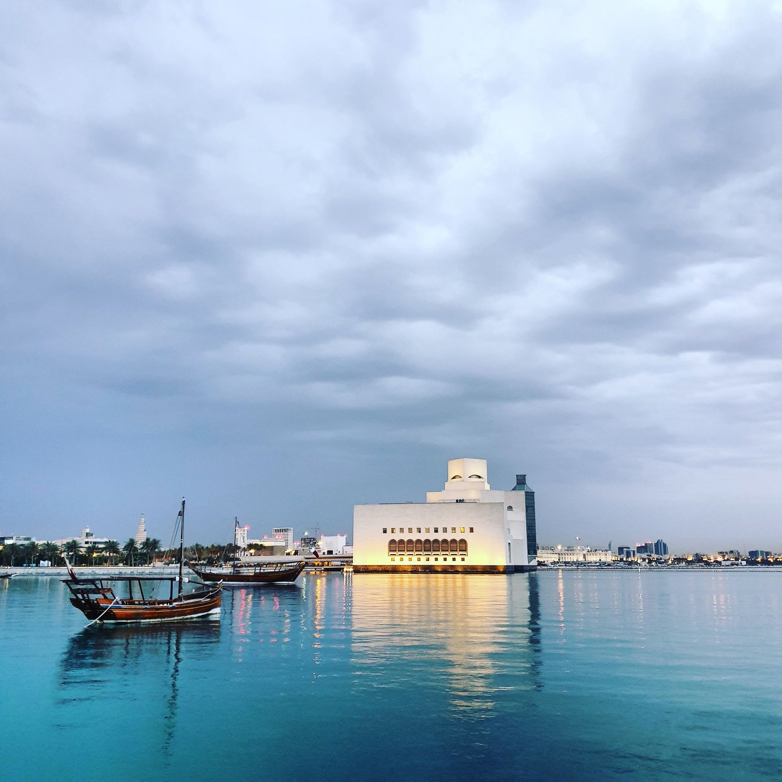 Scenery view of contemporary house facade reflecting in river with floating boats under sky in town in evening