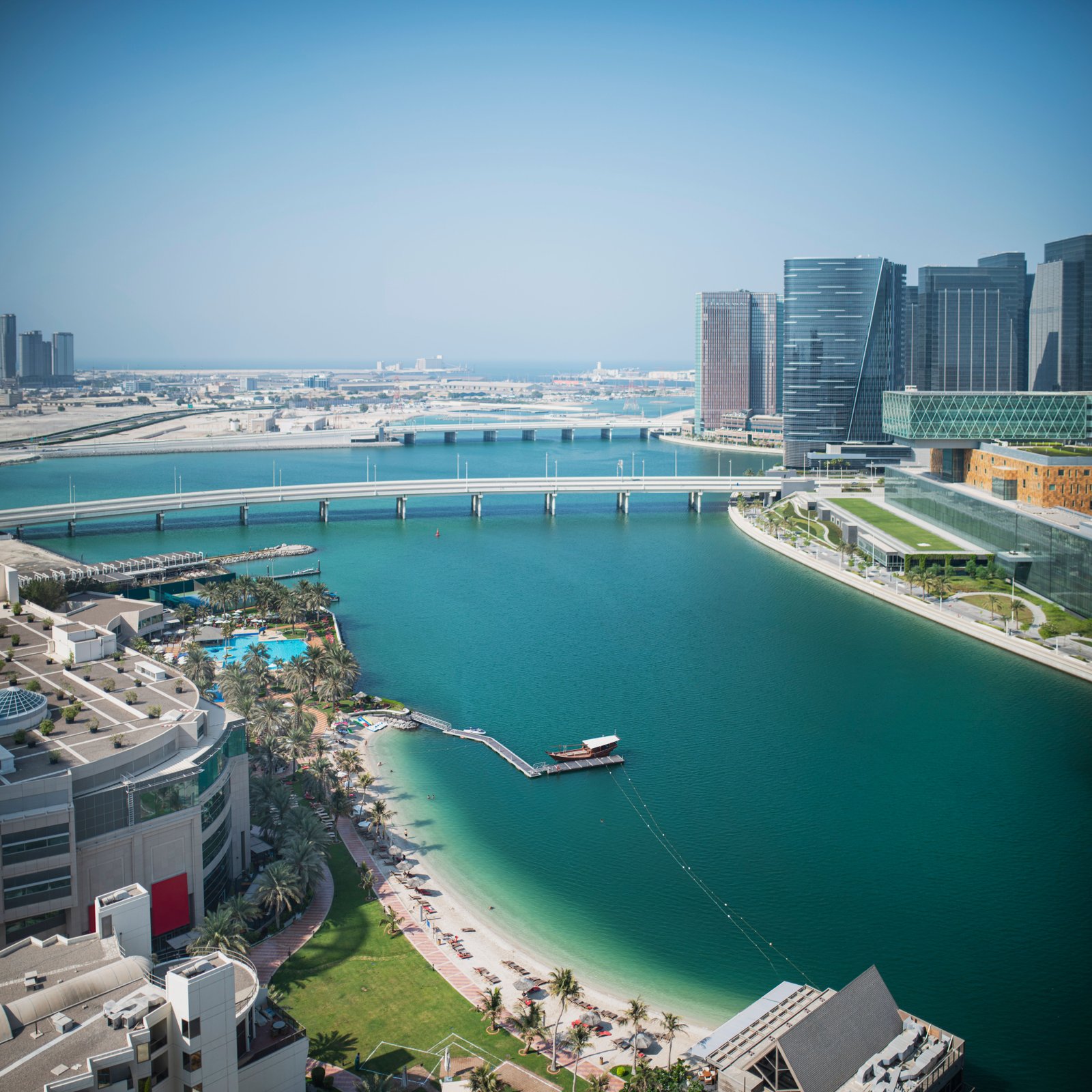Cityscape of modern skyscrapers located near calm water in harbor on summer sunny day under blue cloudless sky