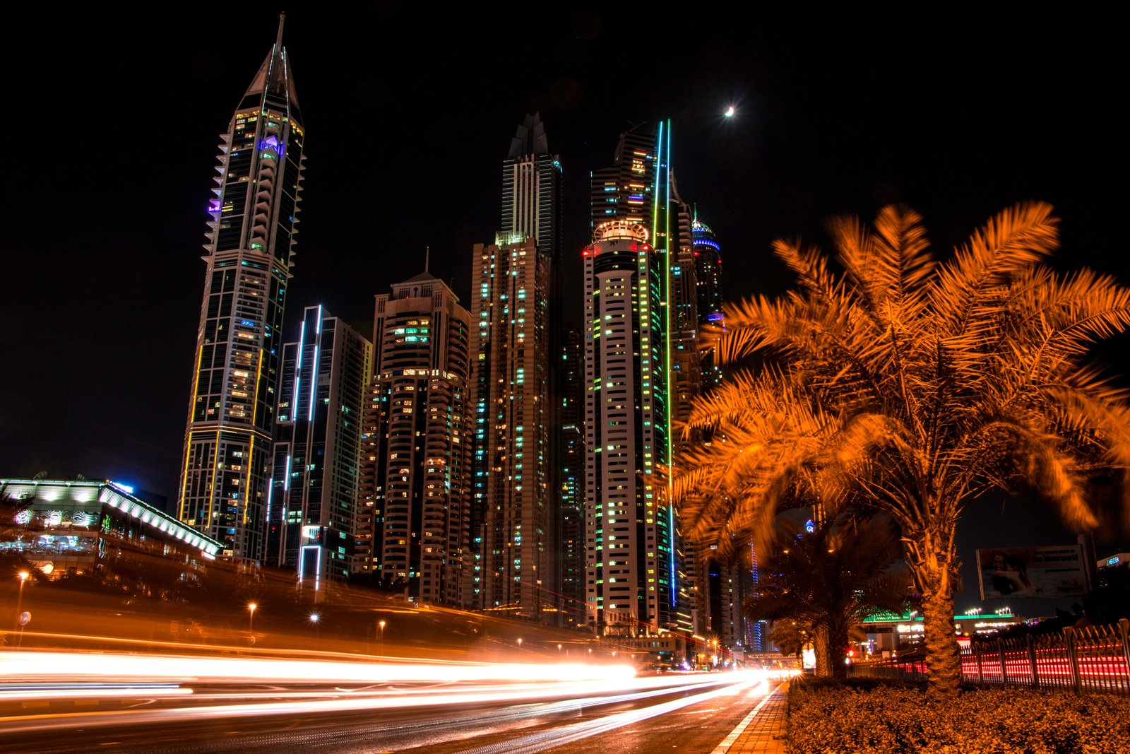 Stunning night view of Dubai's illuminated skyscrapers and palm trees with light trails from passing cars.